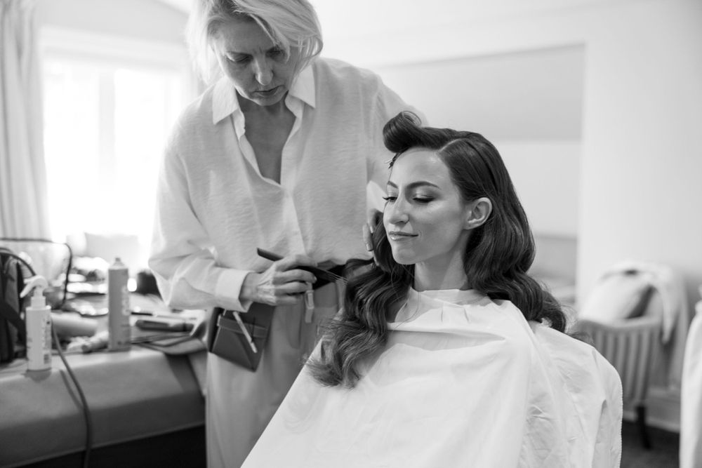 Black and white photo of a hair styling session with a stylist working on a client wearing a white salon cape.