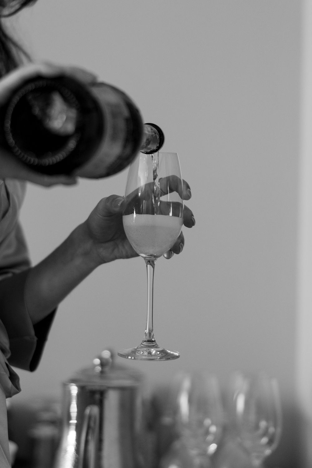 A hand pours white wine into a glass in black and white monochrome.
