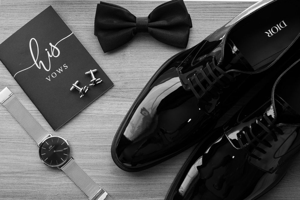 Black bow tie and formal shoes arranged with gift boxes on a gray wooden surface for elegant menswear styling.