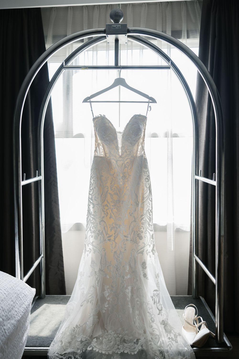 Elegant white lace wedding dress hanging in window light creating a romantic silhouette display.