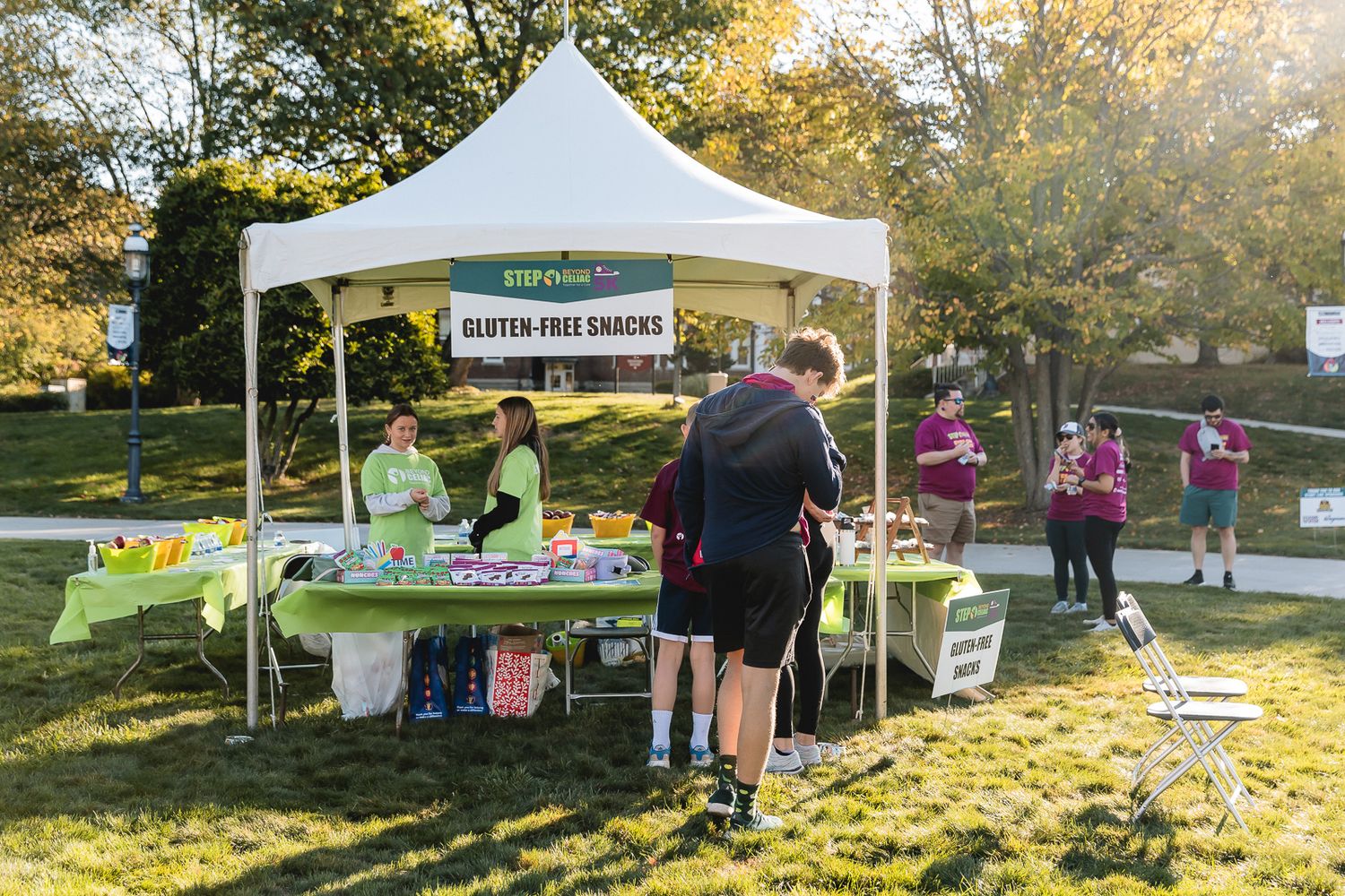 Outdoor event booth with white tent canopy selling fresh produce at a farmers market on a sunny autumn day.