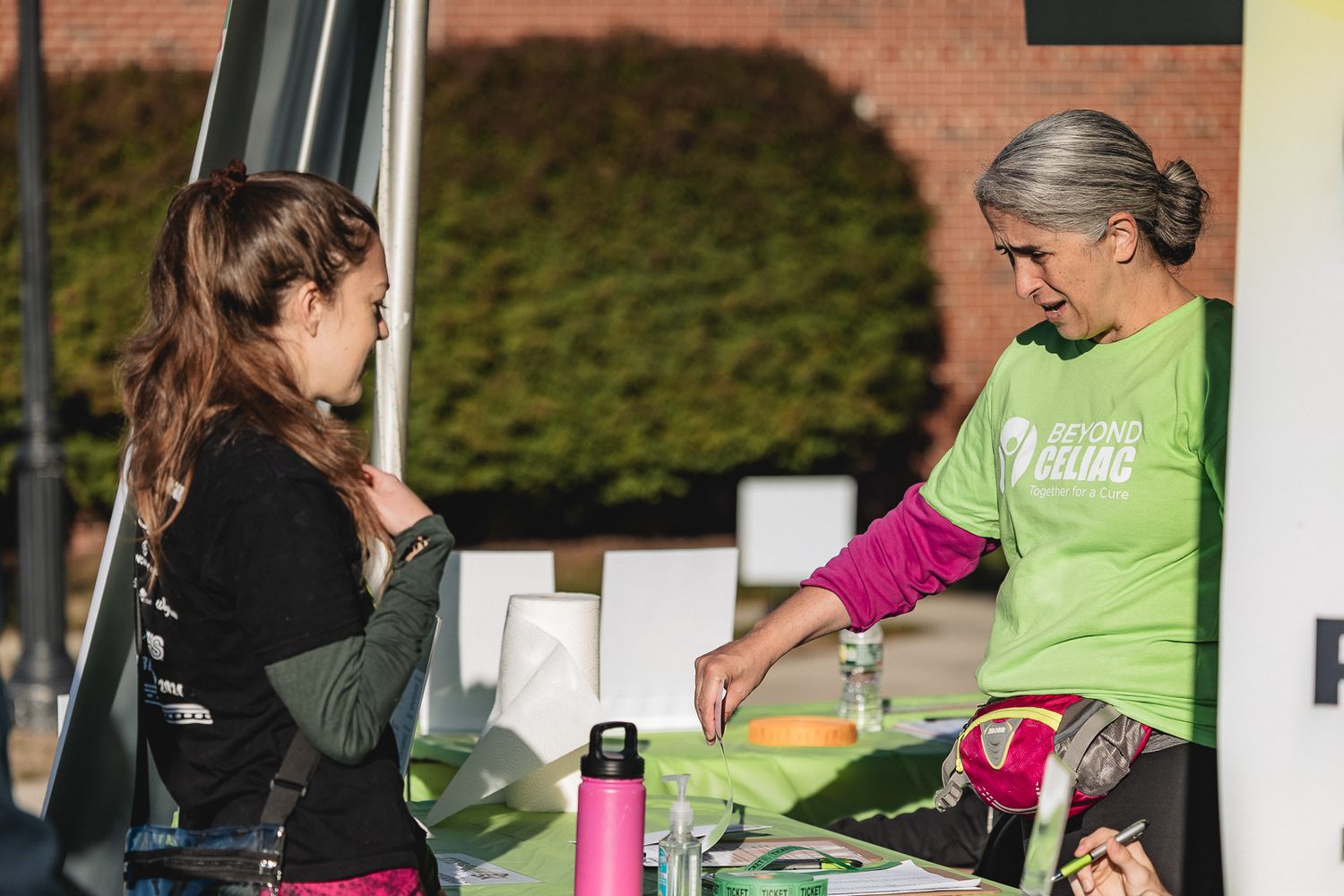 People gathered around a table outdoors with pink and green clothing participating in a community activity.