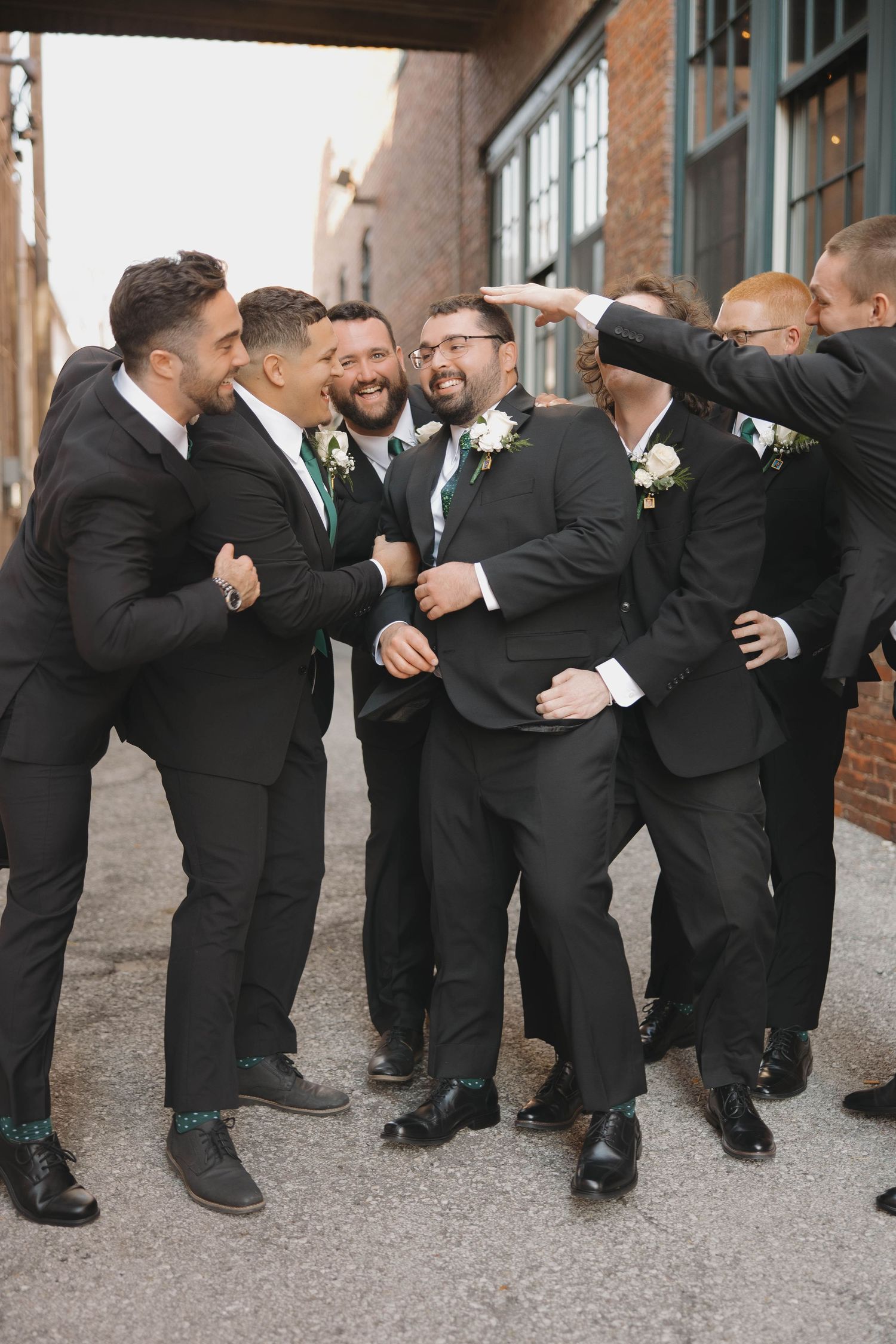 Groomsmen in black suits line up for a fun group photo showing their colorful socks.