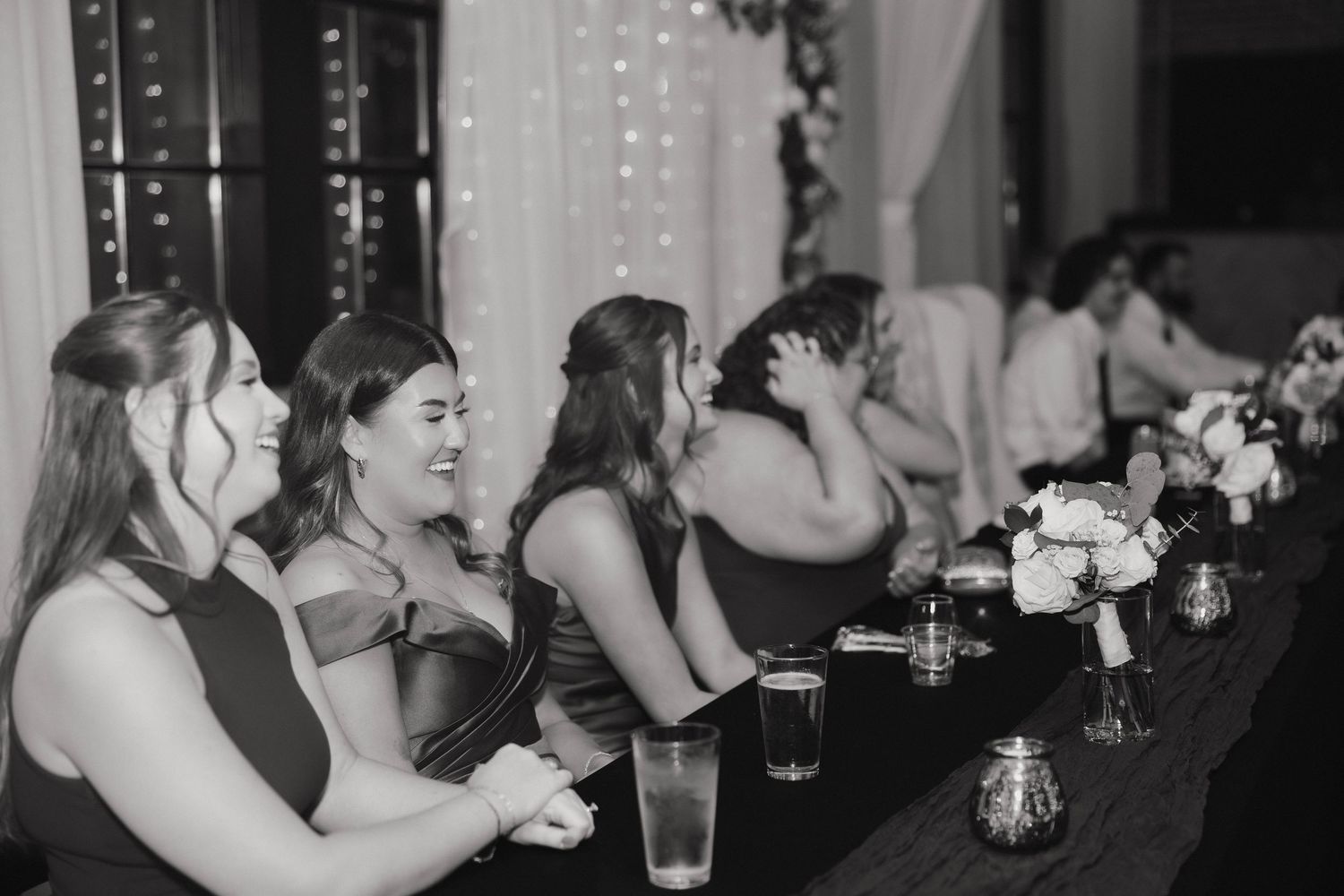 Wedding reception guests enjoy drinks and conversation at dimly lit tables with string lights.