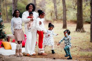 A family wearing white outfits walks together through a wooded area during an outdoor photo session.