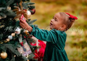A person in a green sweater and red hat throws colorful autumn leaves into the air during a fall photo session.