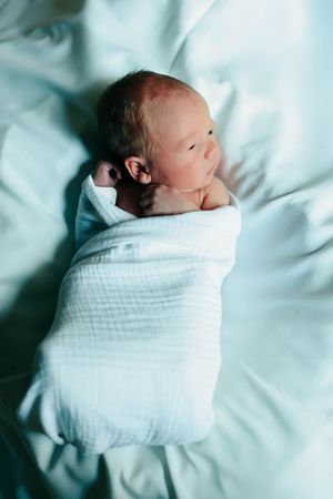 Newborn baby swaddled in white blanket lying on light blue bedding shown in progressive stages.