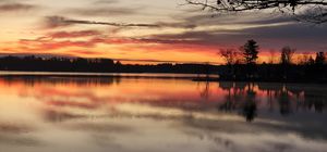 Panoramic sunset view over a lake with silhouetted trees reflecting on calm waters.