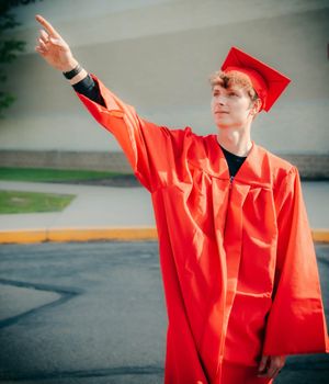 Graduate in bright red cap and gown poses against grey background.