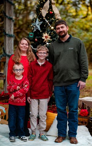A family in festive red sweaters and jeans poses for Christmas photos outdoors in front of winter decorations.