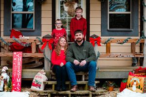 A group sits on a porch decorated with red holiday stockings and festive Christmas decor at sunset.