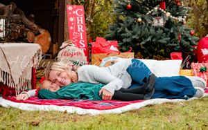A cozy outdoor Christmas scene with someone resting on a blanket near a decorated tree and holiday decor.