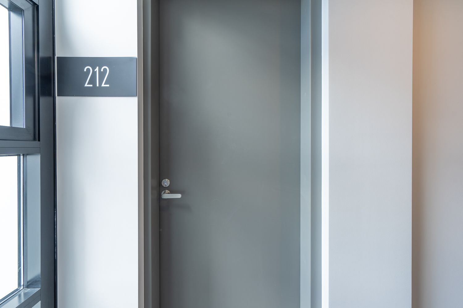 Modern grey apartment door numbered 212 with sleek silver handle in contemporary hallway.