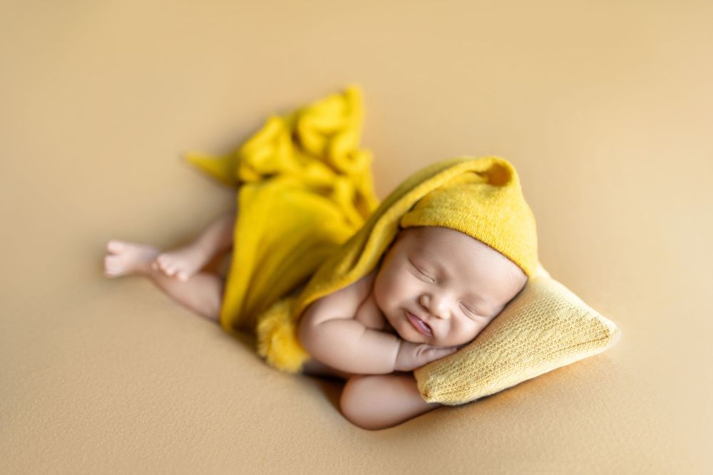 A sleeping baby wrapped in soft yellow blankets lies peacefully on a beige background.