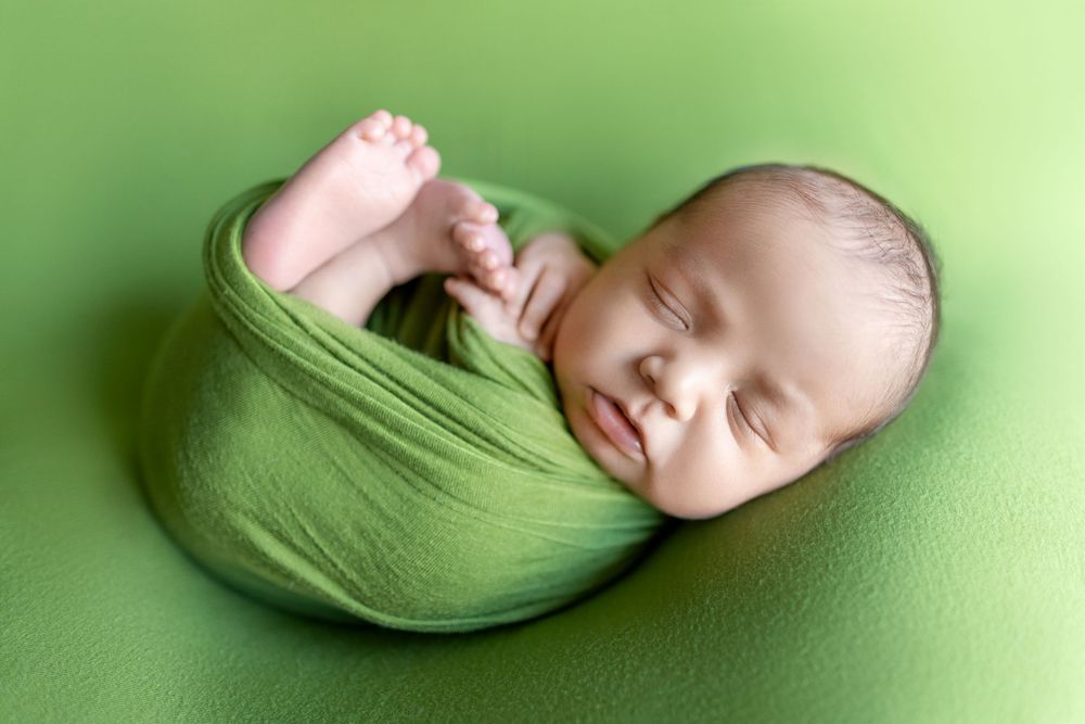 Peaceful sleeping newborn wrapped in soft green fabric against matching green background.