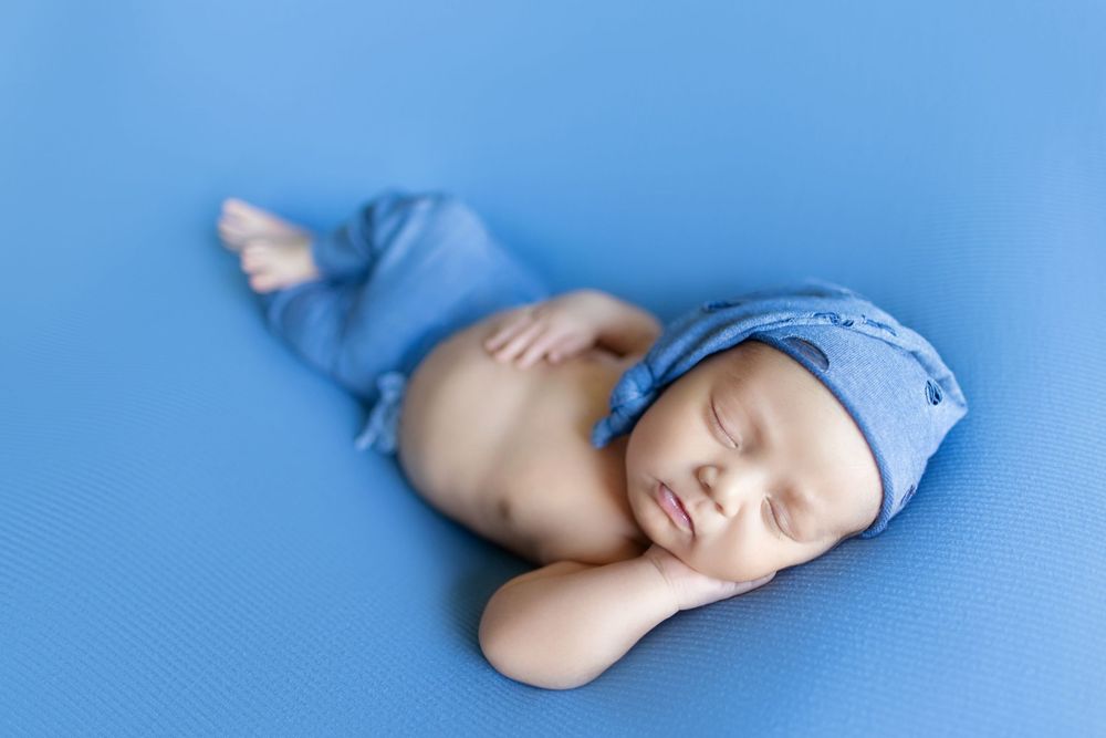 A sleeping baby in a blue onesie lies peacefully on a light blue background in a series of connected photos.