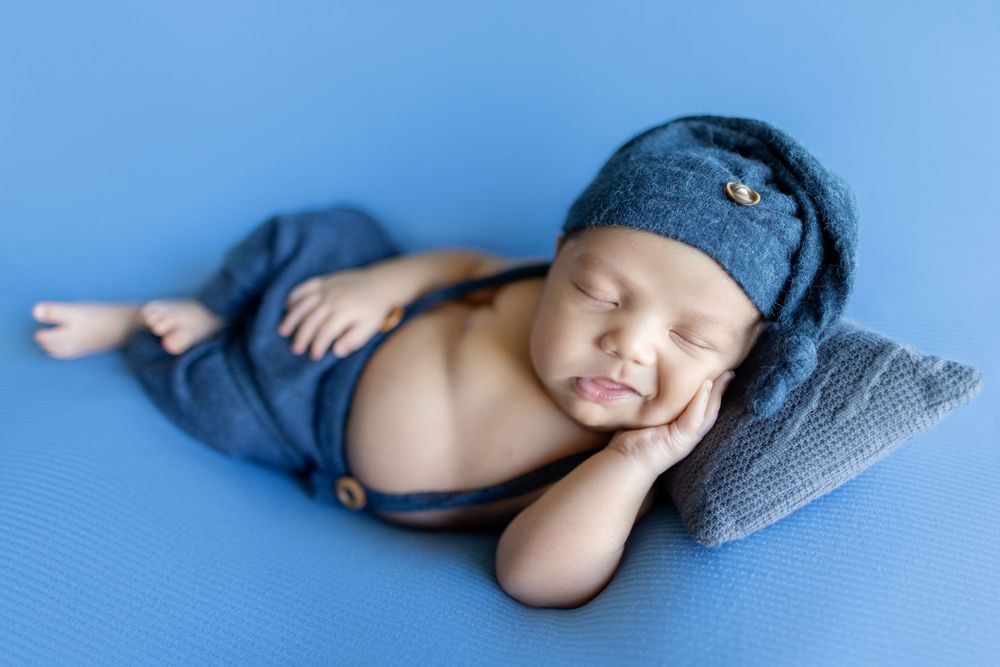 Sleeping newborn baby wrapped in gray blanket on blue background photographed from multiple angles.