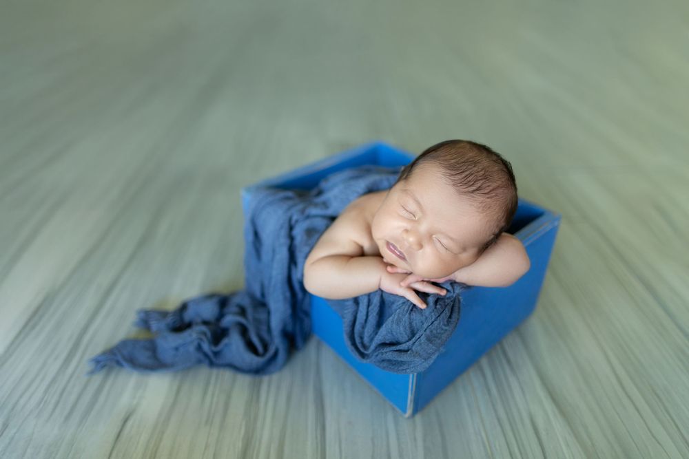 A sleeping baby in blue clothing lies on a light-colored wooden floor.