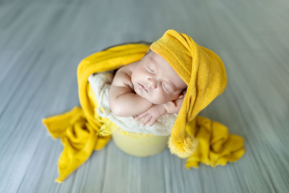 A newborn baby wrapped in a soft yellow blanket sleeps peacefully during a professional photo session.