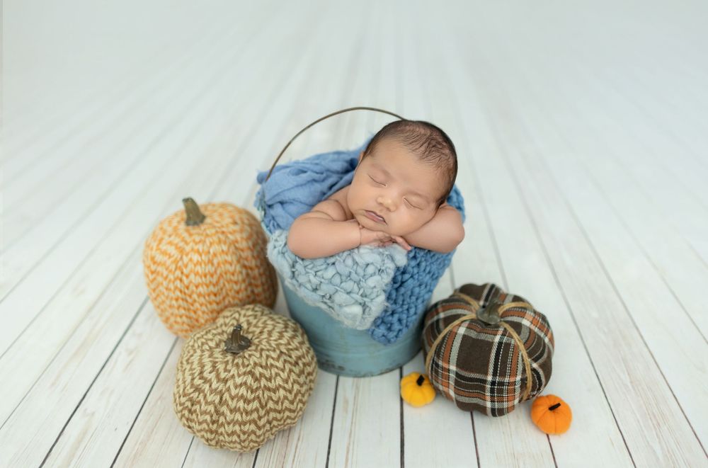 A collection of newborn photography props including knit pumpkins, plaid caps, and soft blankets on white wooden floors.