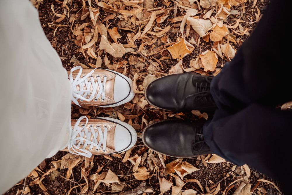 White sneakers walking through scattered autumn leaves on the ground.