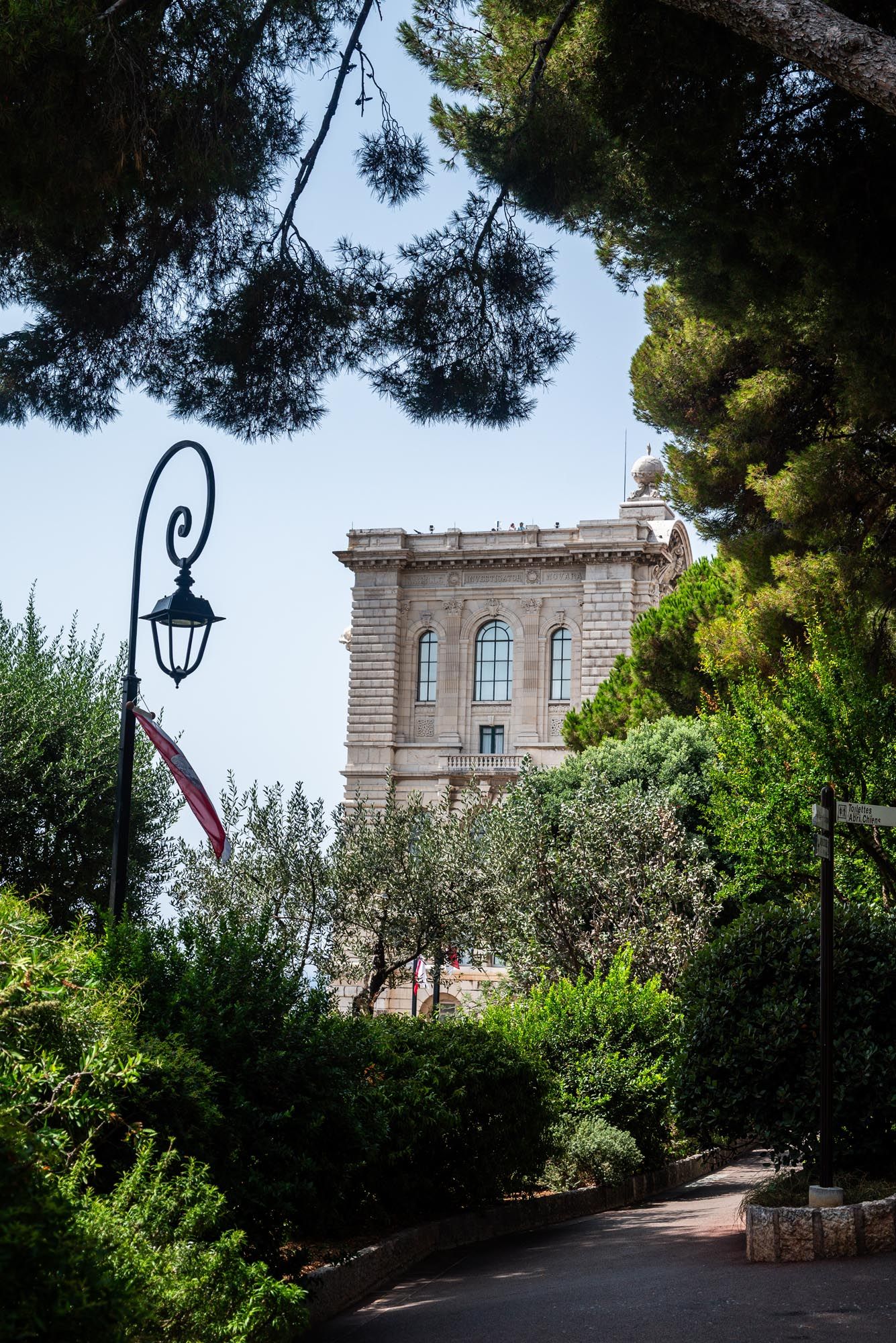 Stone castle walls and towers surrounded by lush Mediterranean gardens and trees along a winding pathway.