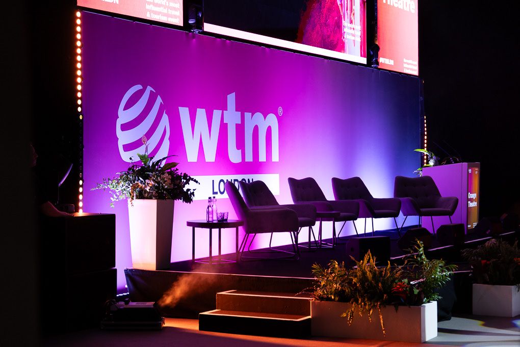 Stage setup at a corporate event with purple lighting and a white WTM logo displayed on a large screen.