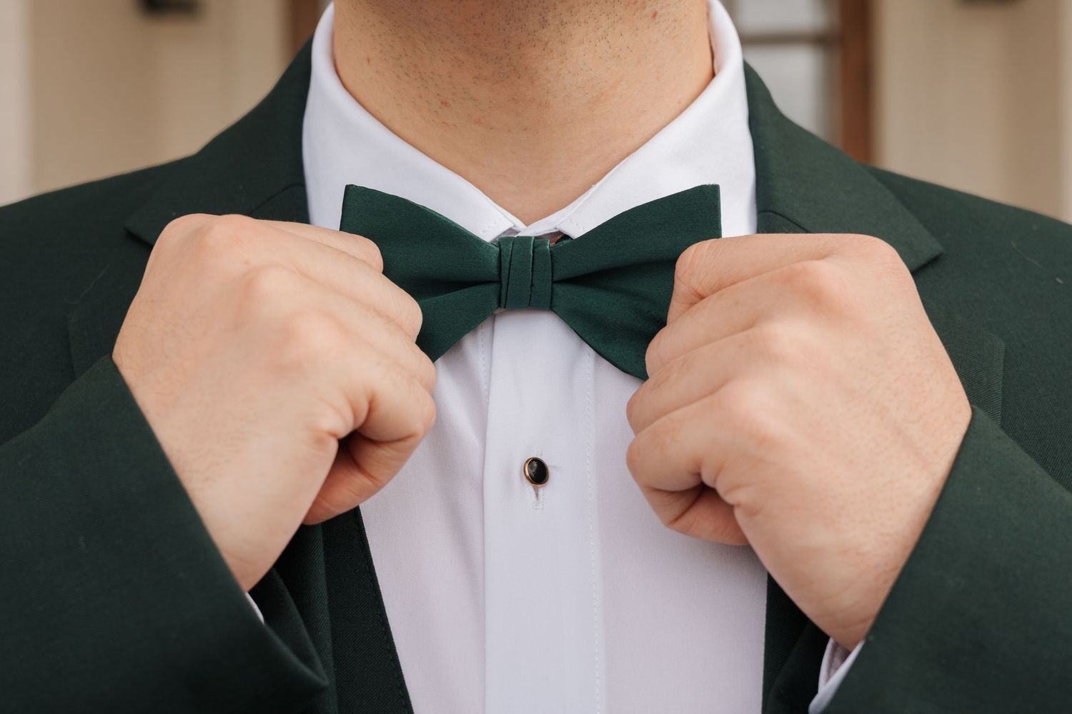 Close up sequence of hands adjusting a black bow tie against a white dress shirt and dark green jacket.