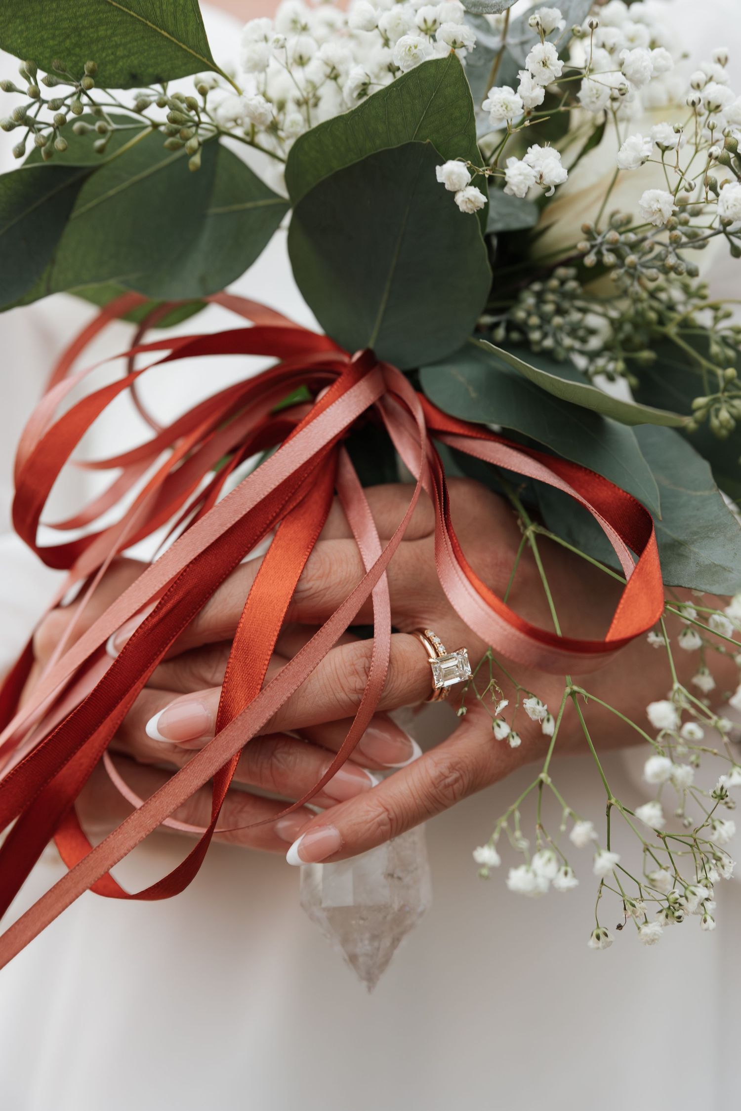 A diamond engagement ring sparkles among red ribbons, eucalyptus leaves and baby's breath flowers in a wedding detail shot.