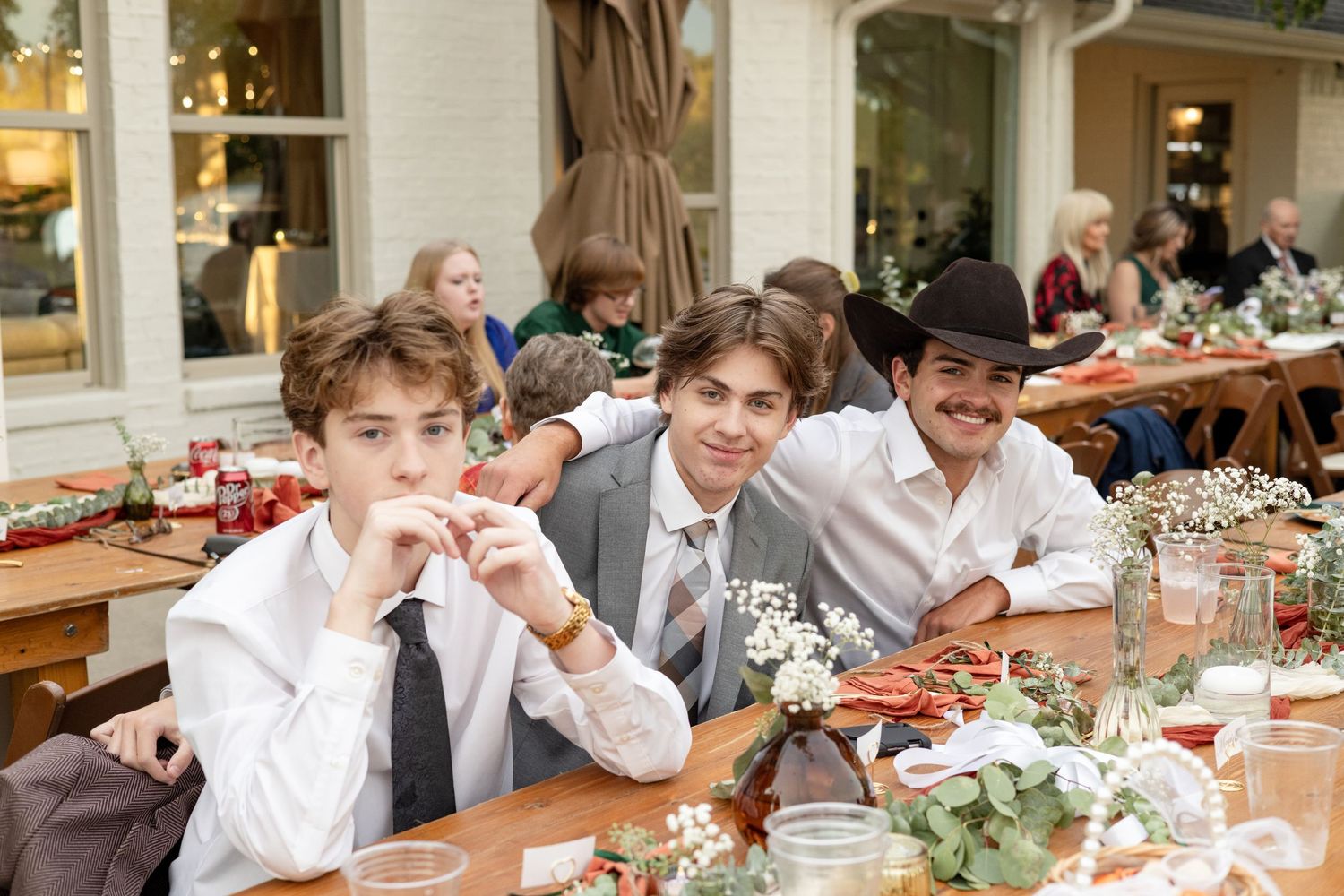 Young guests in formal attire seated at an elegant wedding reception table with floral centerpieces and place settings.