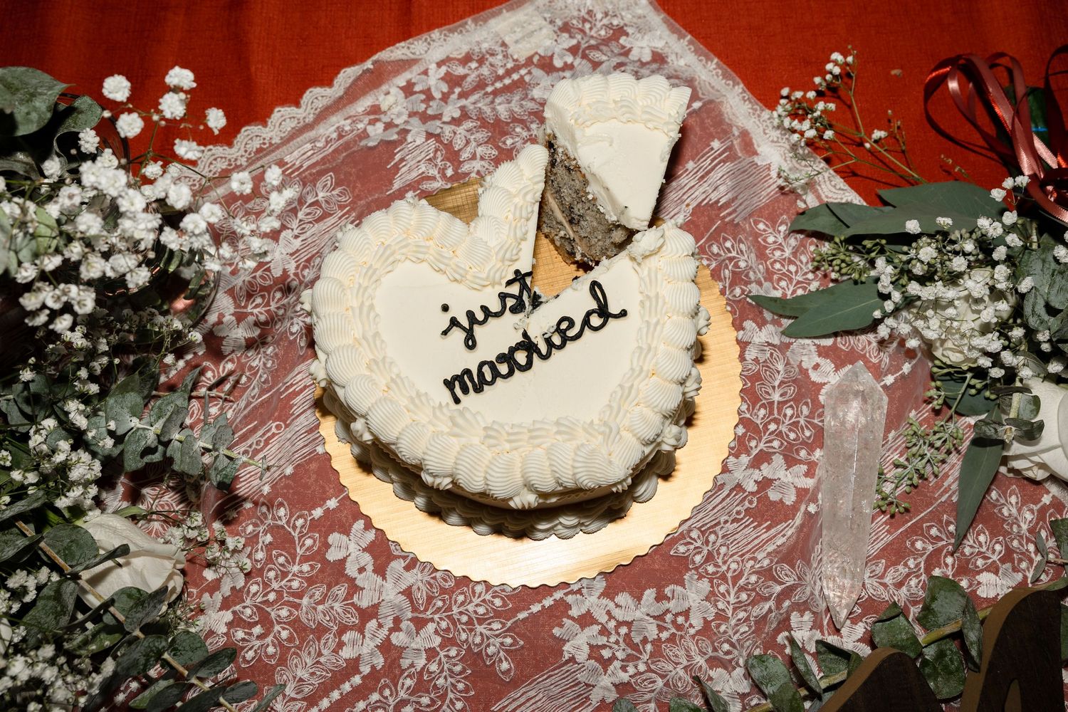 A heart-shaped white wedding cake with 'just married' text sits surrounded by baby's breath flowers and eucalyptus leaves.