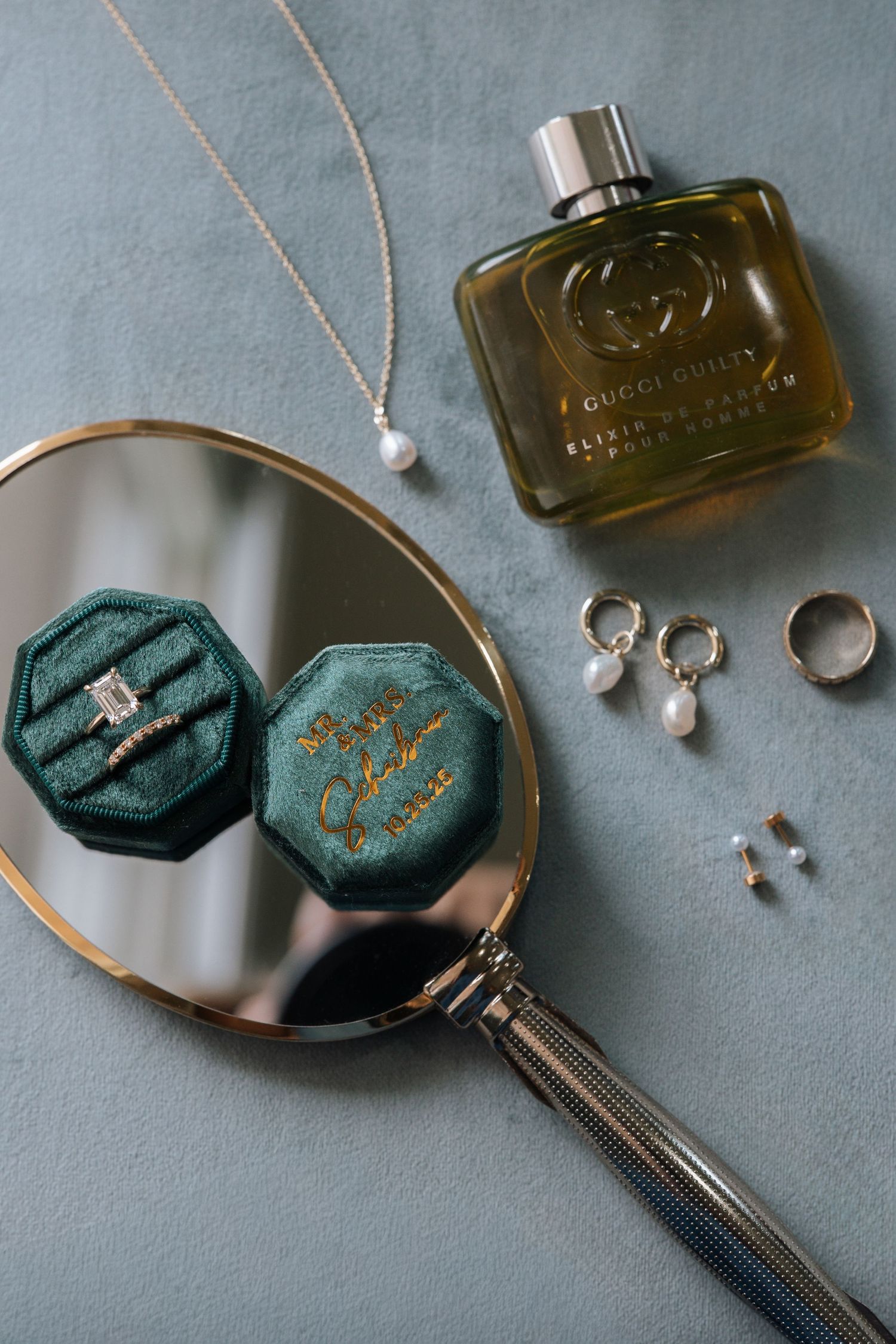 Jewelry styling flatlay with vintage perfume bottle, rings, necklaces and green velvet trinket boxes on gray surface.