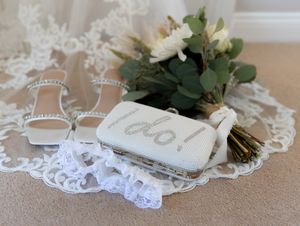 White lace wedding garter with delicate floral details and a satin bow displayed on beige fabric.
