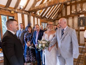 Wedding guests mingle and socialize during a reception in a rustic timber-framed venue with exposed wooden beams.