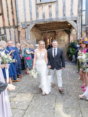 Wedding guests celebrate with confetti on a cobblestone courtyard outside a rustic stone building.