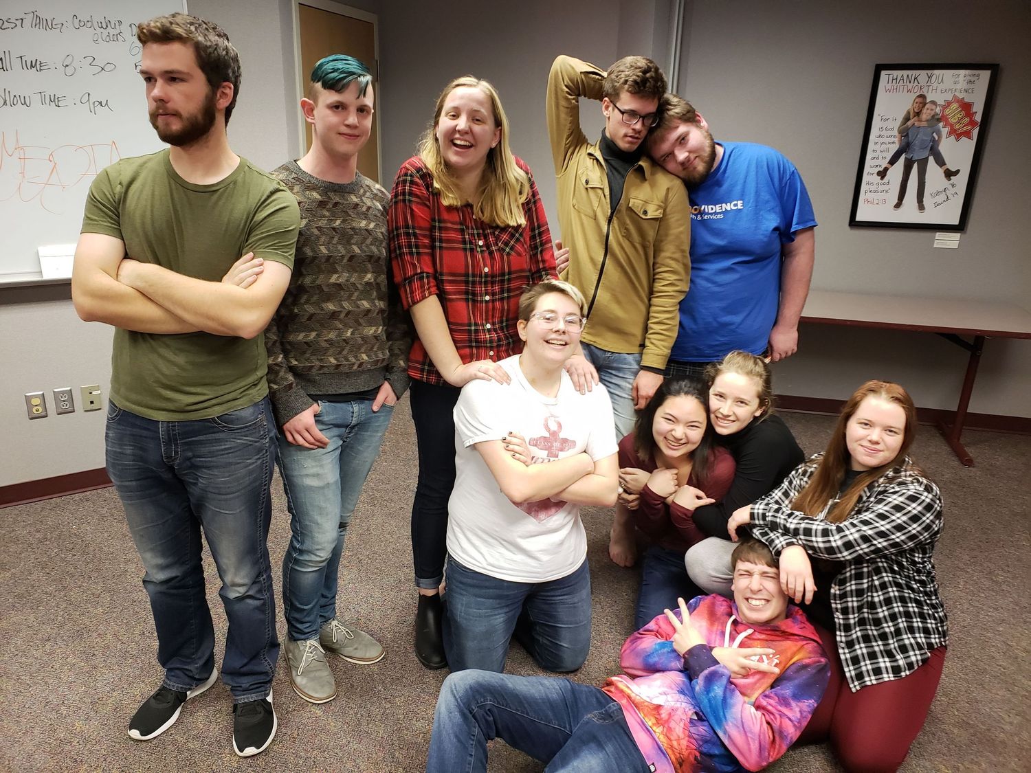 Group of ten smiling college improv comedy performers posing together in a classroom setting.