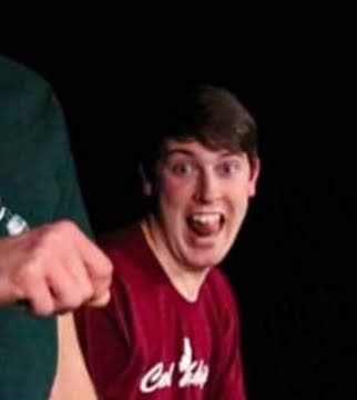 Young male improv comedian performing on stage with an expressive open-mouthed reaction during a show.