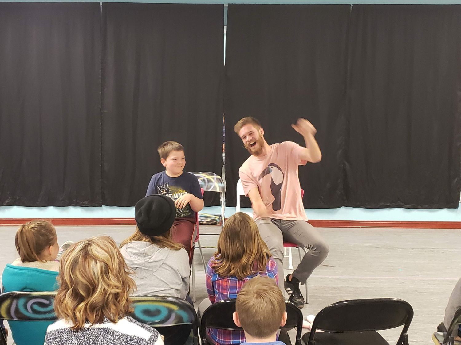 Two energetic performers entertaining a group of children seated in chairs at an indoor event.