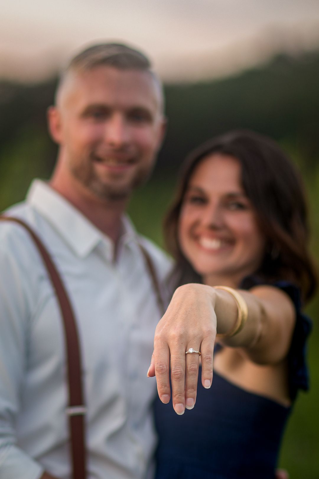 A close-up shot of a person's hand showing off an engagement ring against a blurred background.