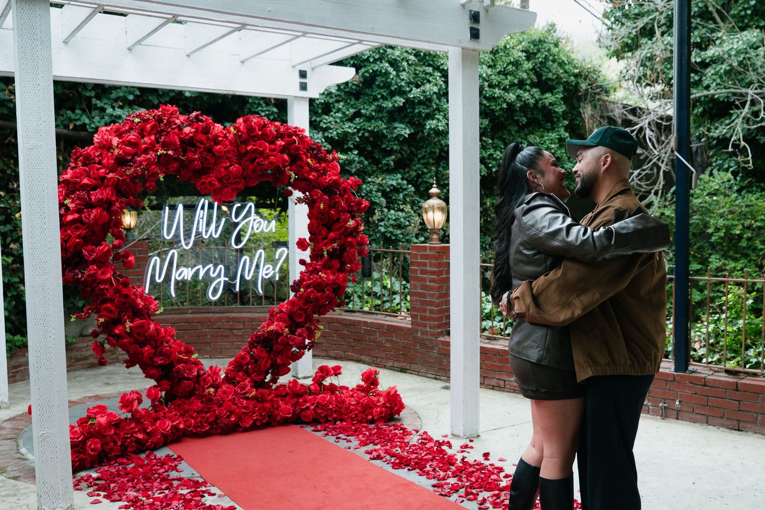 A heart-shaped arch made of vibrant red roses creates a romantic walkway in a garden setting.