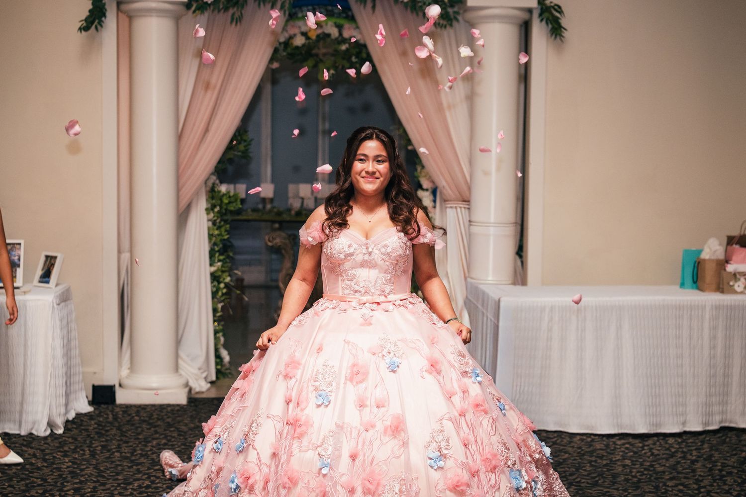 A quinceañera celebration featuring a pink floral ballgown and elegant white columns decorated with holiday greenery.