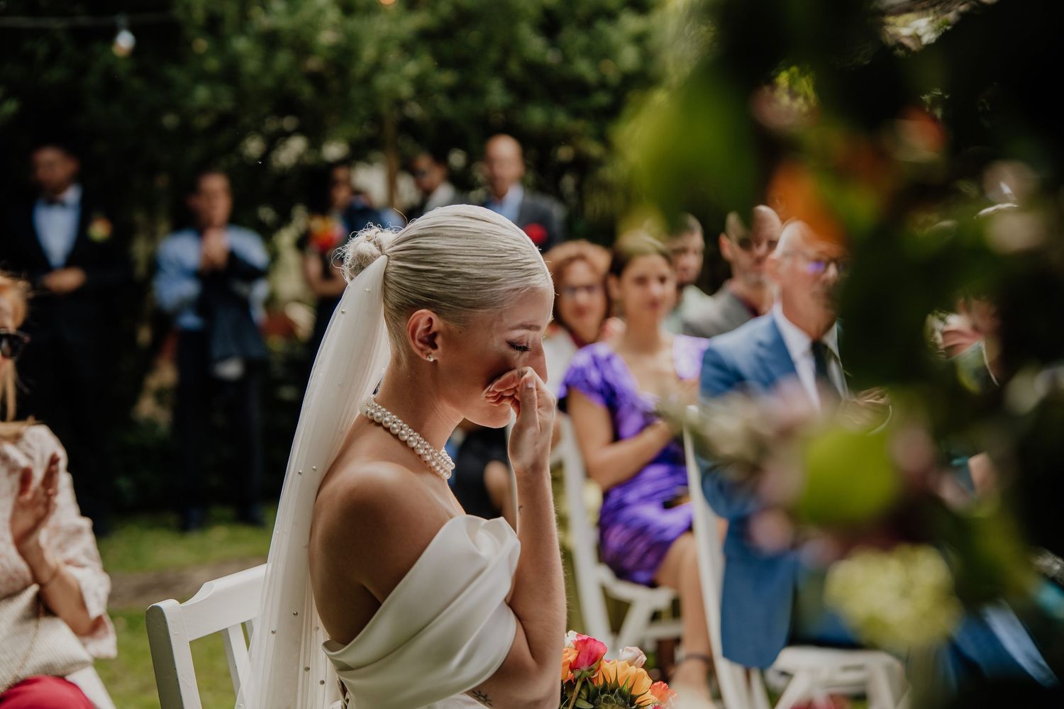 Wedding guests stand and celebrate during an outdoor ceremony while surrounded by lush greenery.