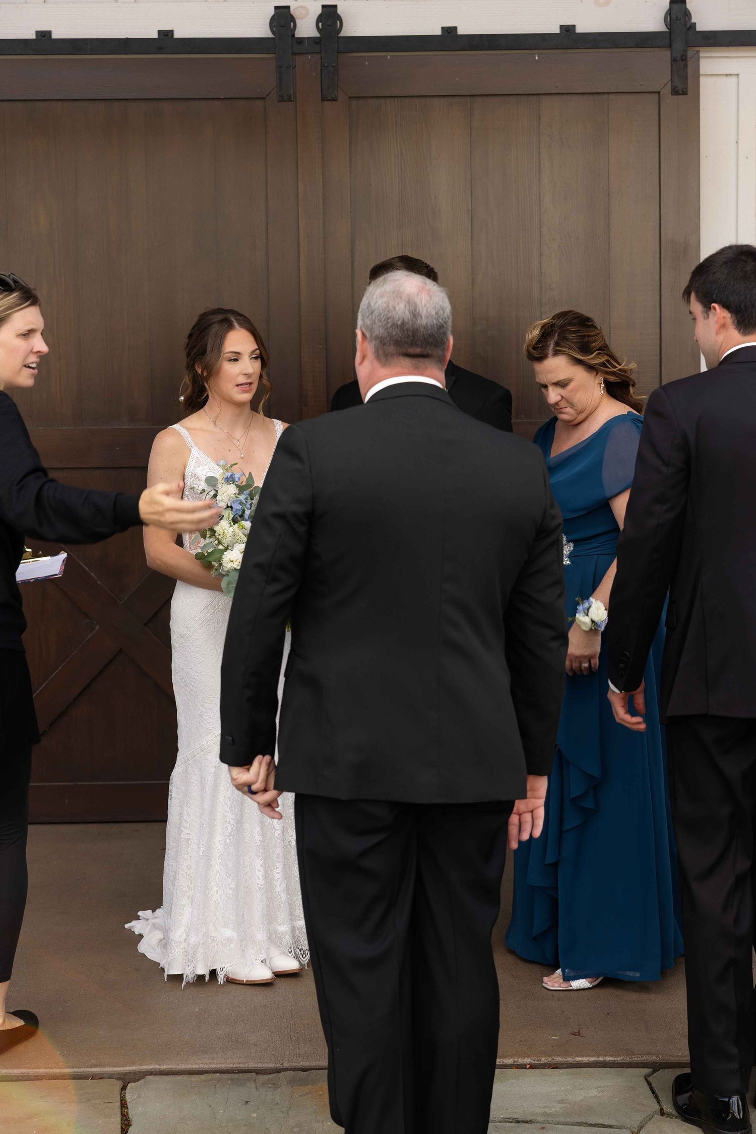 Wedding ceremony taking place in front of rustic brown barn doors with people gathered in formal attire.