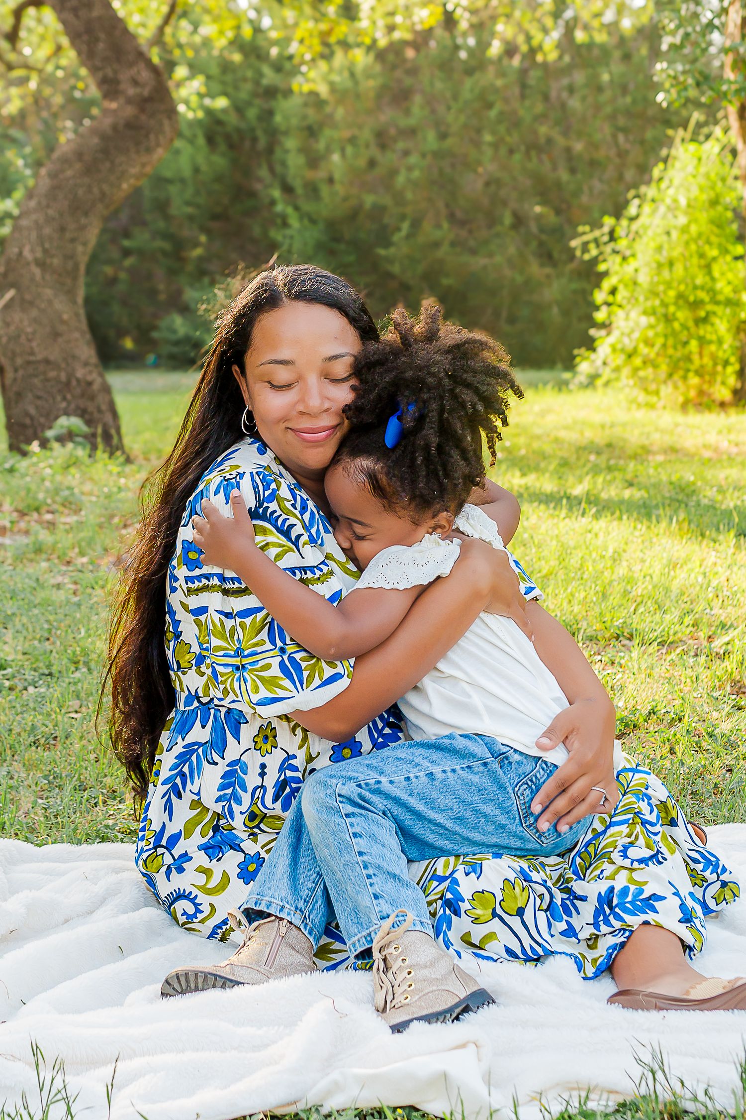 A tender embrace shared on a white blanket in a sunny garden setting with blue floral dresses and denim.