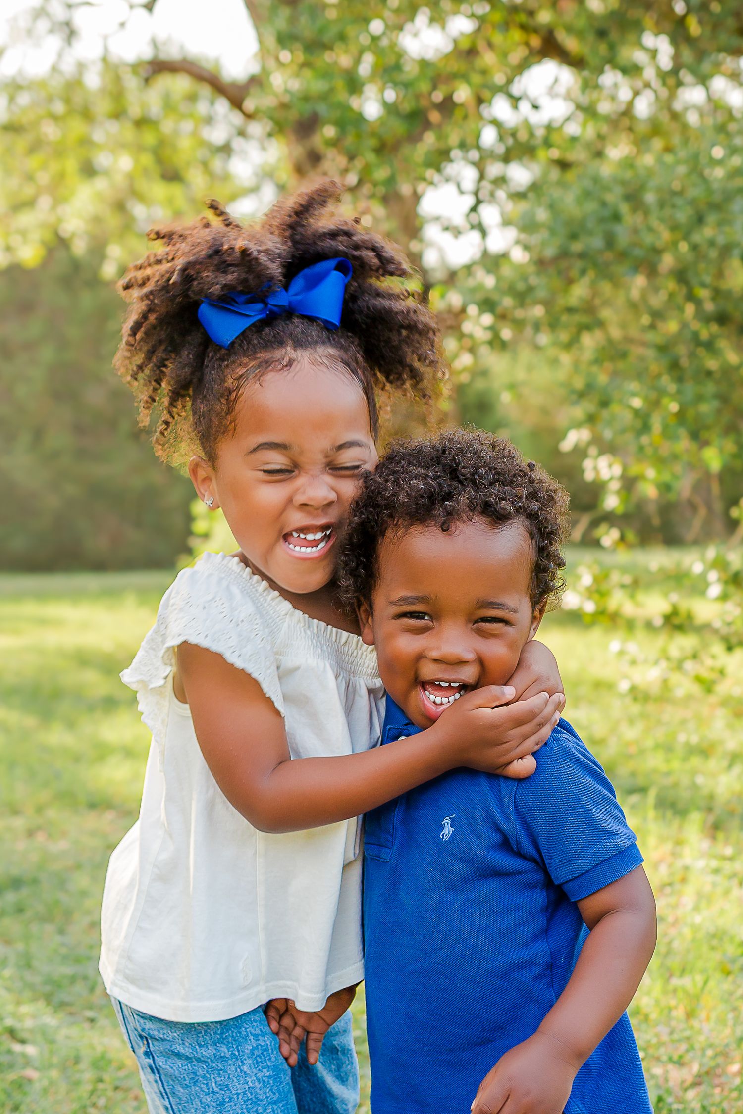Two children share joyful moments together outdoors in a natural setting with autumn trees in the background.