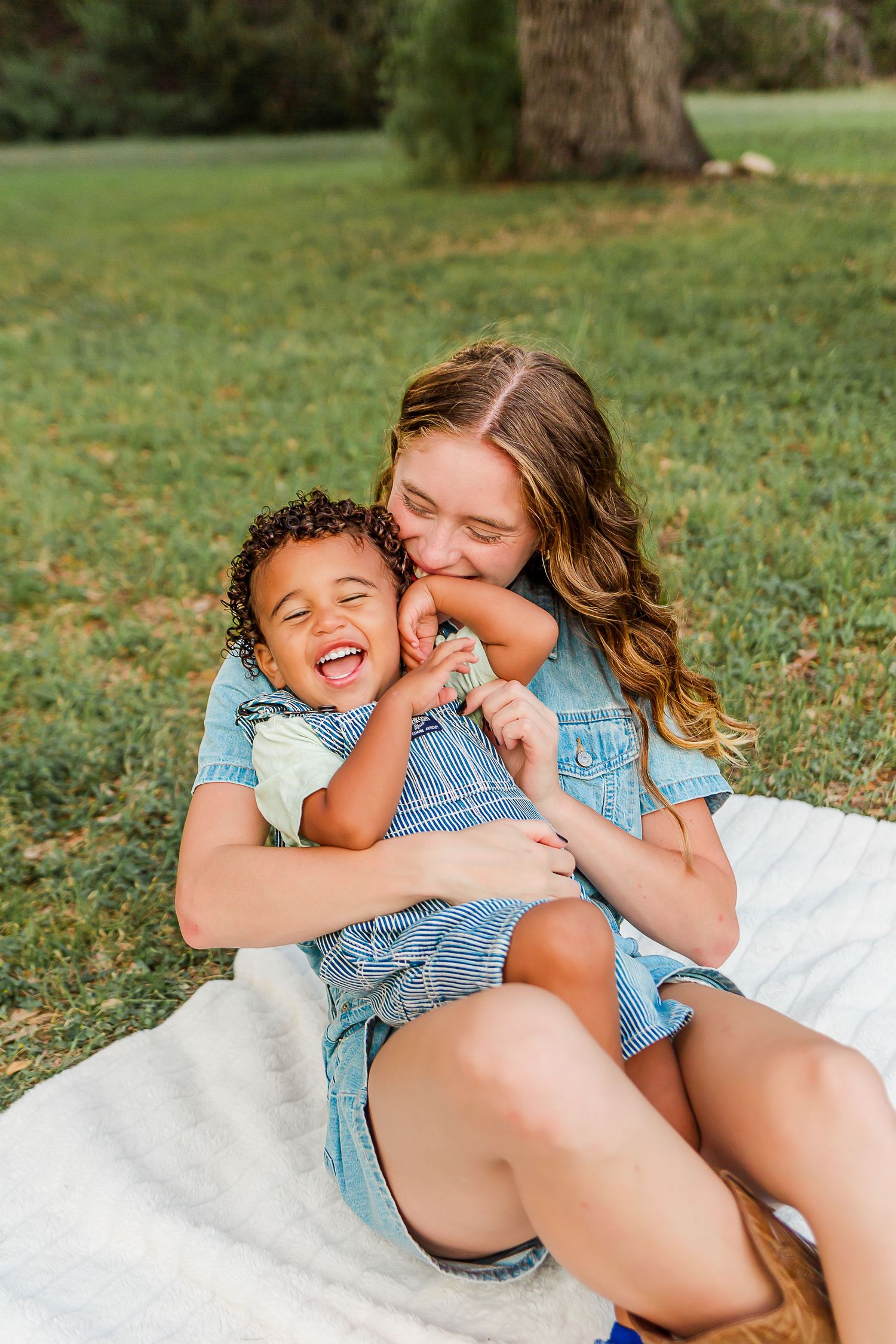 A joyful moment shared between two people wearing denim outfits while sitting on a blanket in the grass.