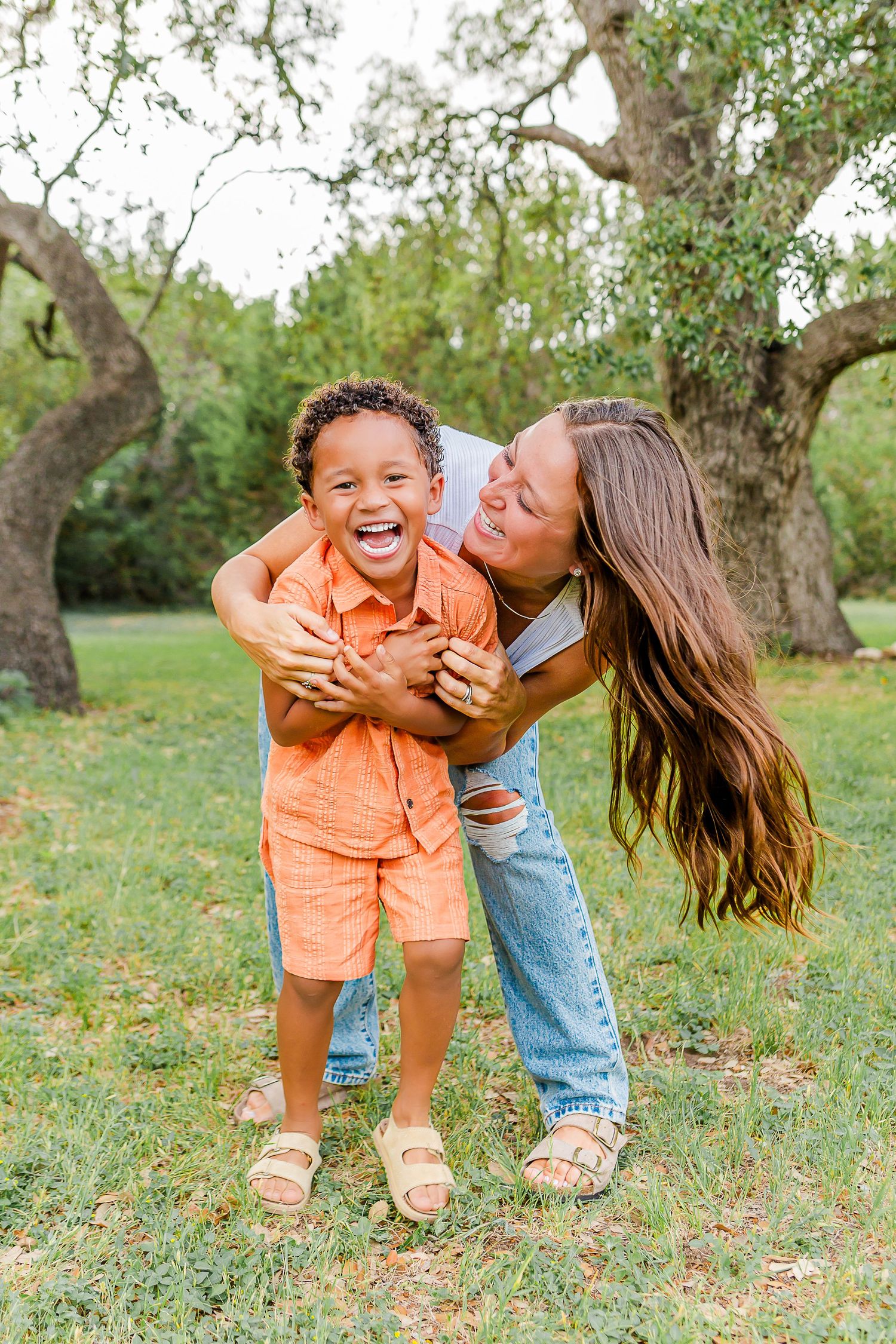 A joyful outdoor family moment captured in a series of candid photos on grassy ground beneath trees.