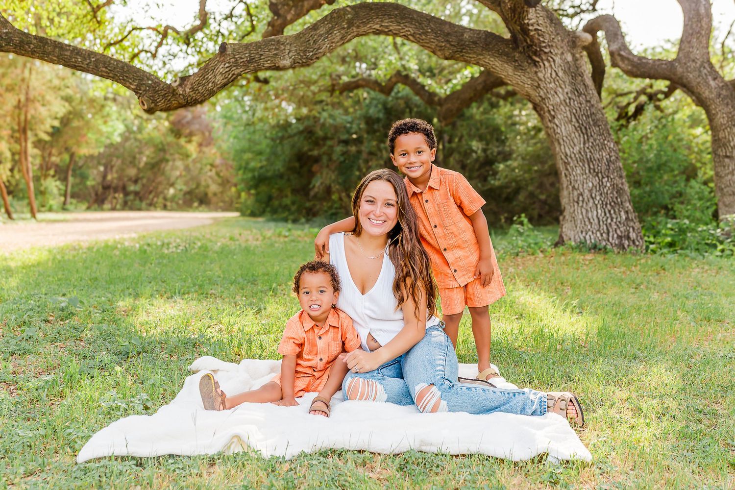 A couple enjoys a romantic picnic together on a white blanket spread out under shady trees in a park setting.