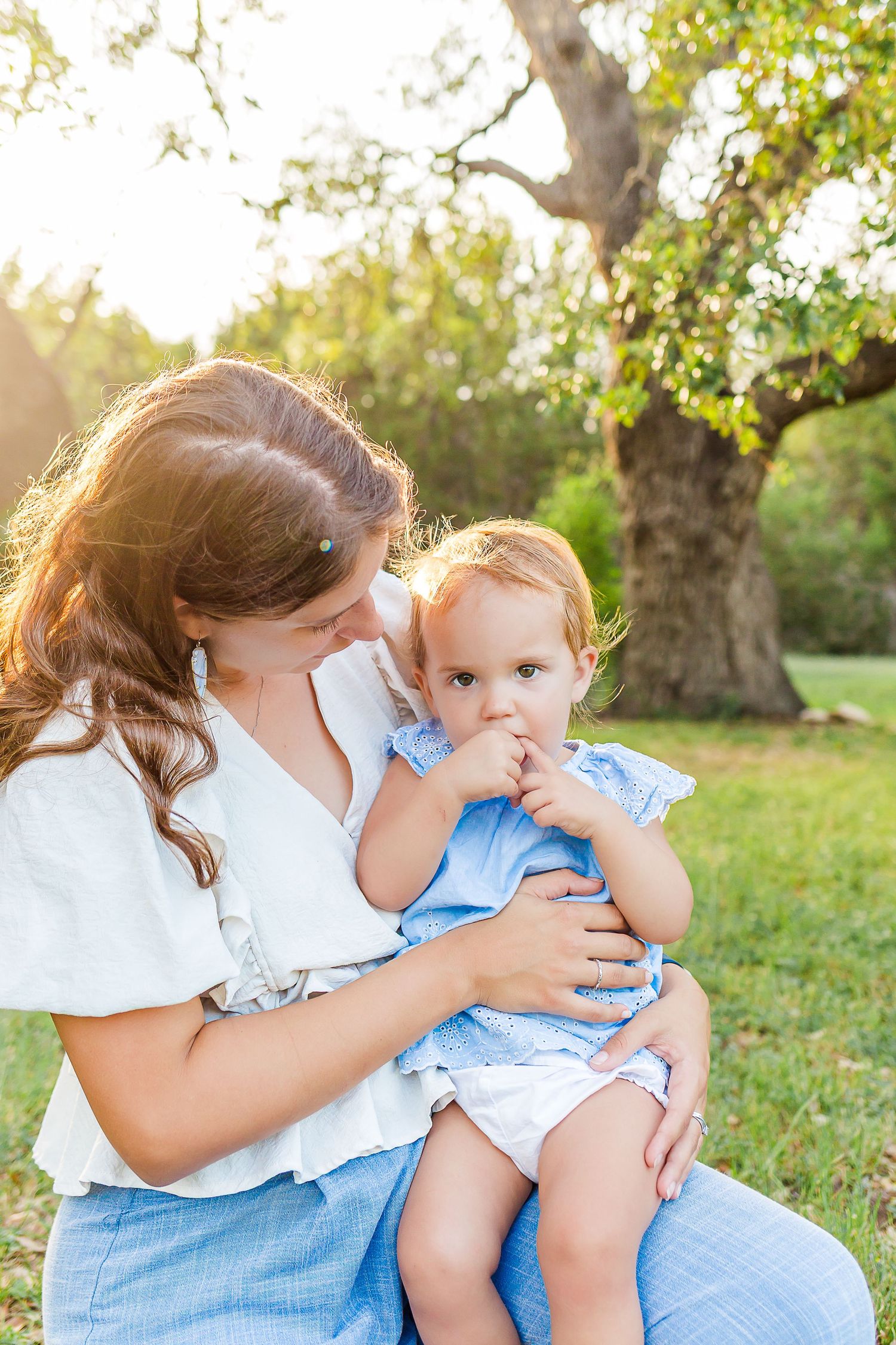 Mother and child in matching white and blue outfits share tender moments in a sunlit garden setting.