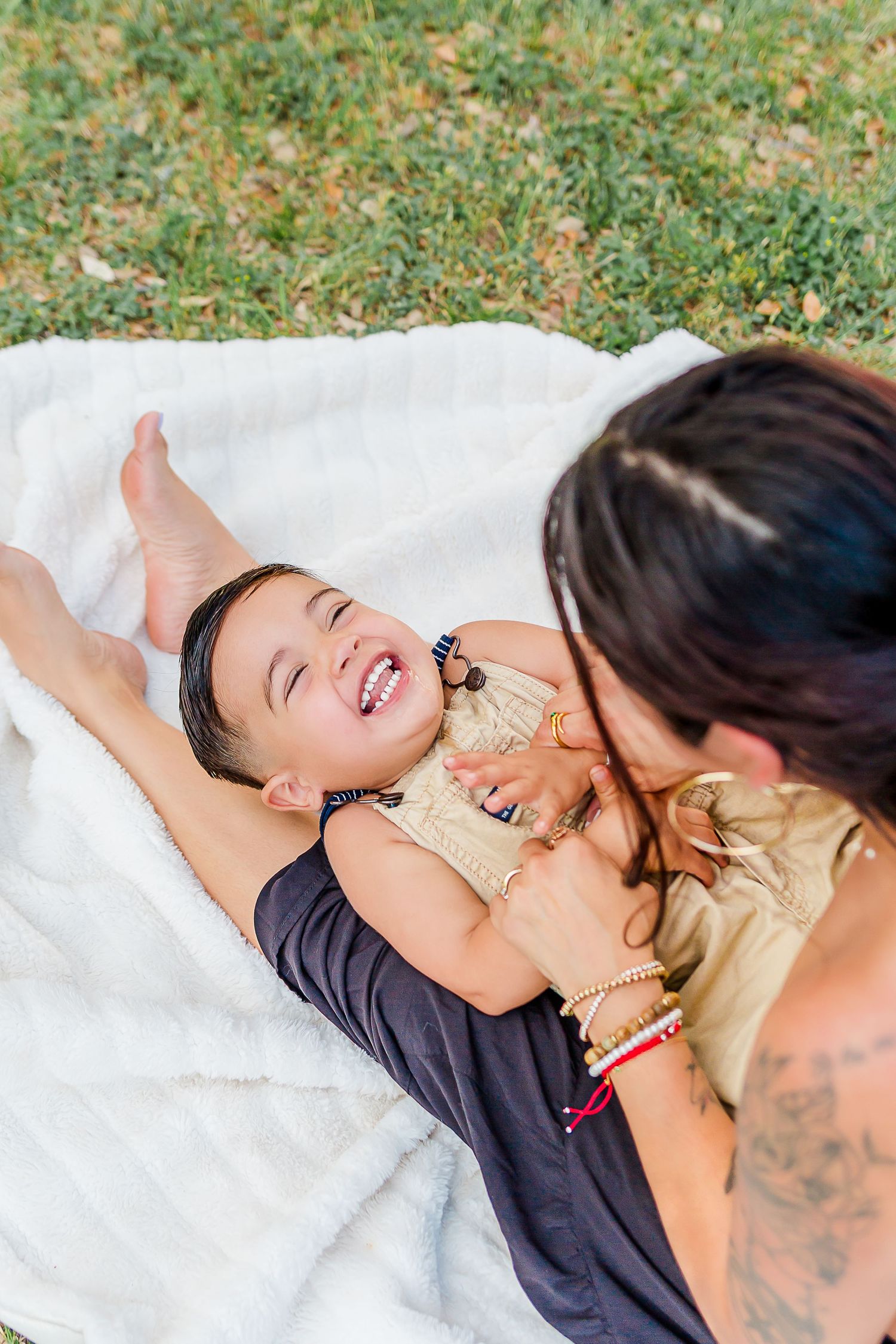 A joyful moment captured on a white blanket in the grass during an outdoor photoshoot.